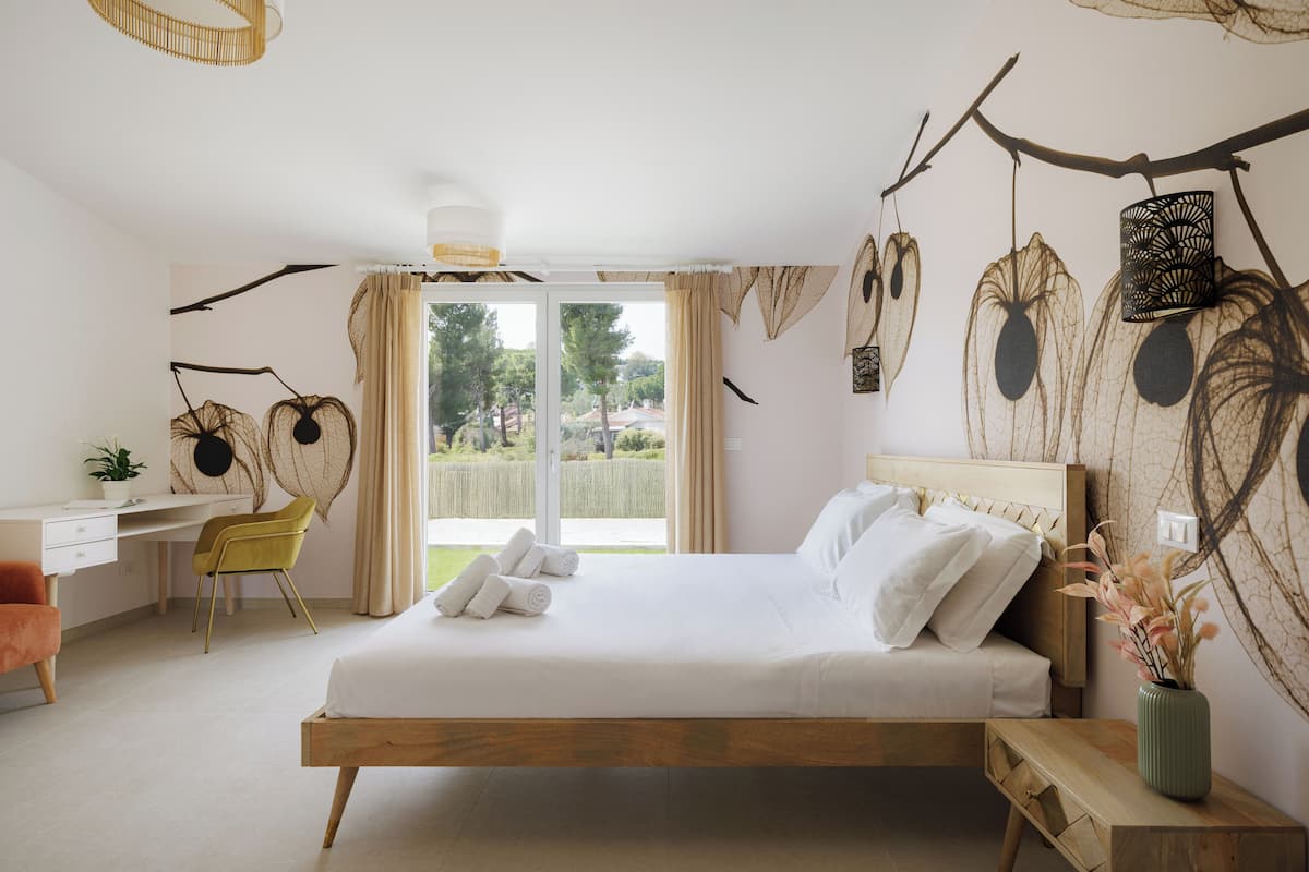 A bedroom with a bed, a desk, a chair, and a view of the outdoors.