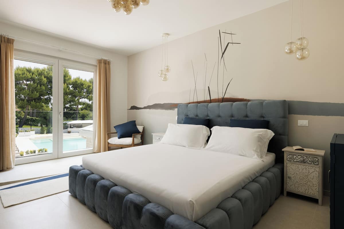 A bedroom with a large bed, a nightstand, a chair, and a view of a swimming pool.