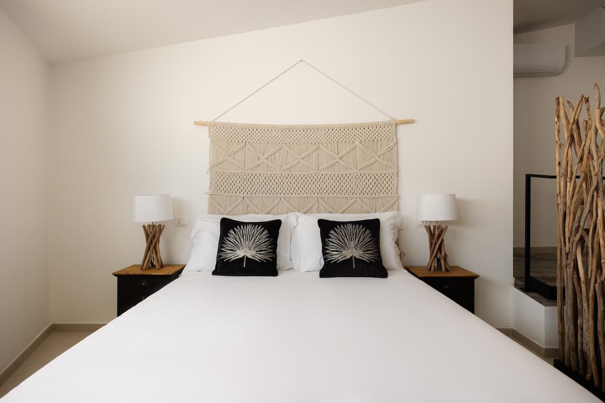 A bedroom with a large bed, two nightstands, a wall hanging, and a wooden decor piece.