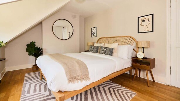 A bedroom with a bed, a bedside table, a lamp, a mirror, and a wall with artwork. - The Waterlow Park Wonder - 2BDR with Study (Greater London)