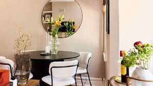 A dining area with a round table, white chairs, a round mirror, and vases with flowers. - The Waterlow Park Wonder - 2BDR with Study (Greater London)