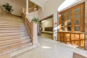 Una gran escalera con peldaños de mármol que conduce a un rellano, un mostrador de recepción de madera y un amplio ventanal con múltiples divisiones.