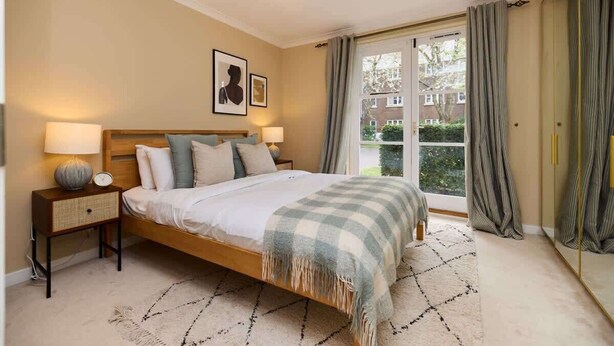Een slaapkamer met een bed, twee nachtkastjes, een raam met gordijnen en uitzicht op buiten.