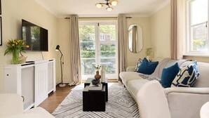 Een woonkamer met een bank, een salontafel, een televisie, een radiator en een raam met gordijnen.