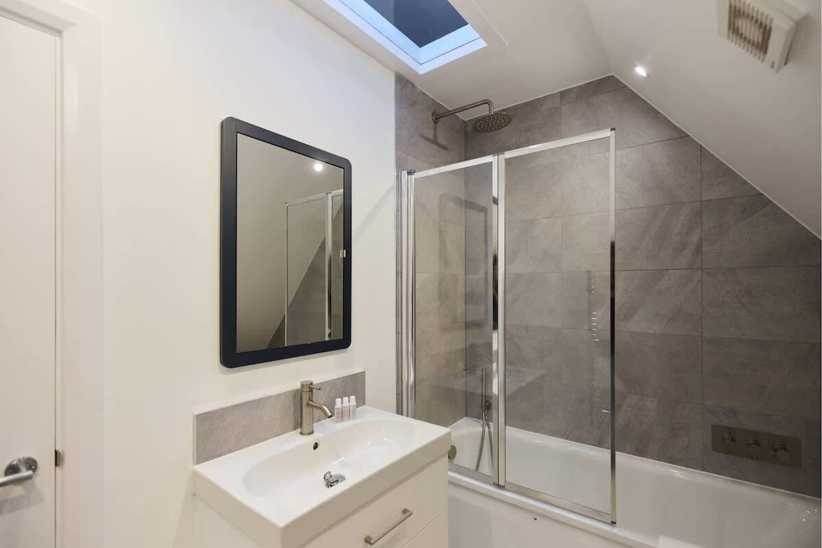 A modern bathroom with a skylight, a large mirror, a shower enclosure, and a bathtub.