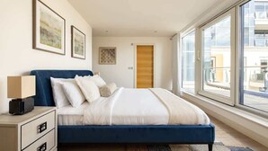A bedroom with a bed, bedside table, lamp, and artwork on the wall.