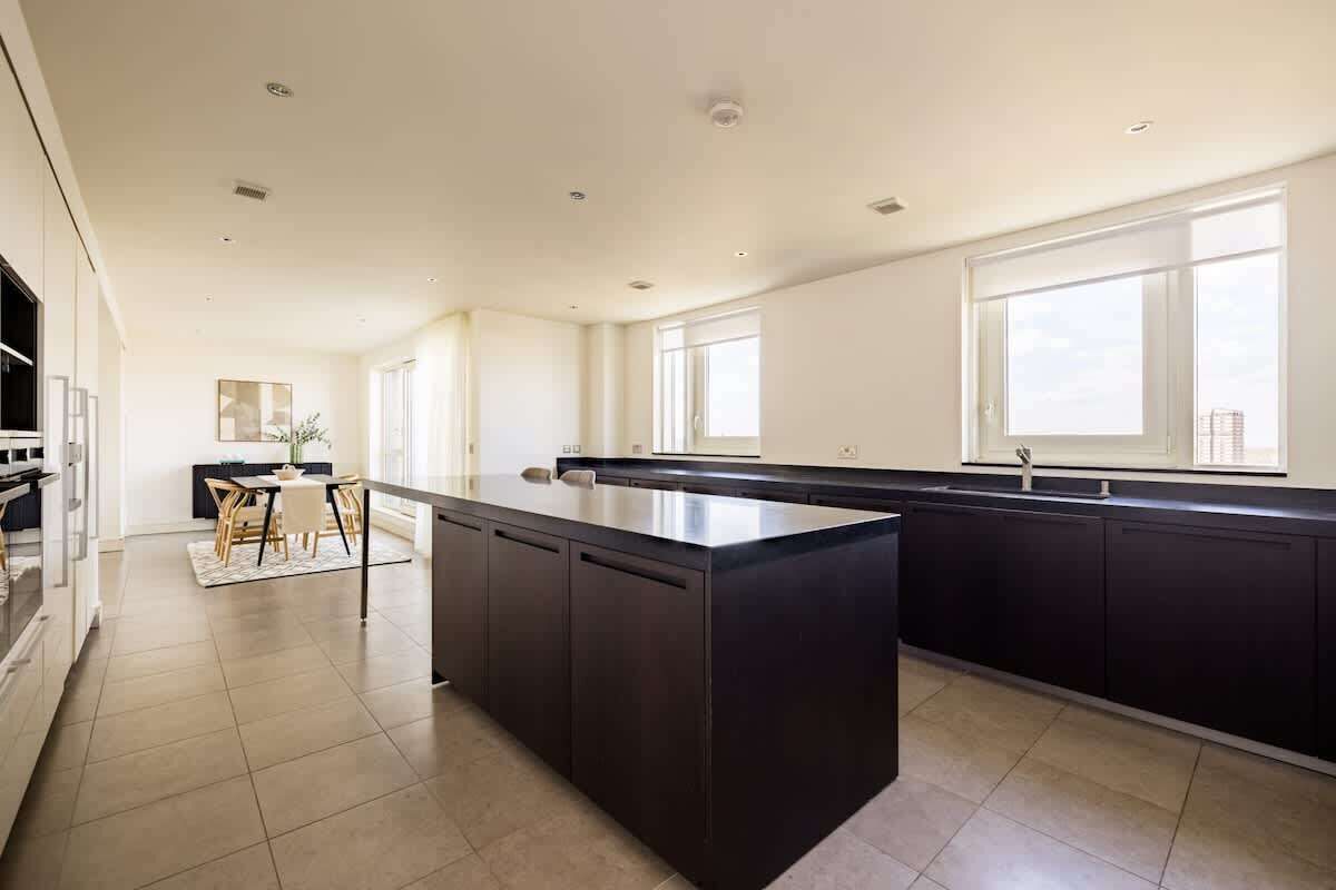A modern kitchen with a central island, dark cabinetry, and large windows.