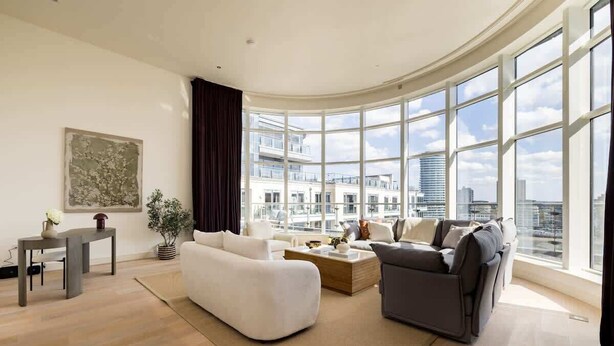 A spacious living room with a large window, a sofa, a coffee table, and a small table with a vase.