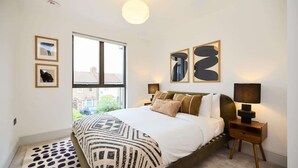 Une chambre à coucher avec un lit, une fenêtre, une table de chevet et des œuvres d’art murales.