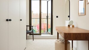 Une pièce dotée d’une porte-fenêtre coulissante donnant sur un balcon, d’un bureau en bois, d’une chaise et d’un petit miroir rond.