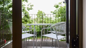 Un balcon avec une table et des chaises en métal, une rambarde en métal et une vue sur les arbres.