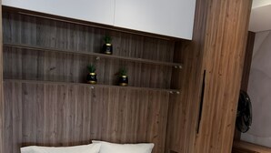 Una cama bien hecha con ropa de cama y almohadas blancas, un cabecero de madera y un pequeño estante con dos plantas en macetas.