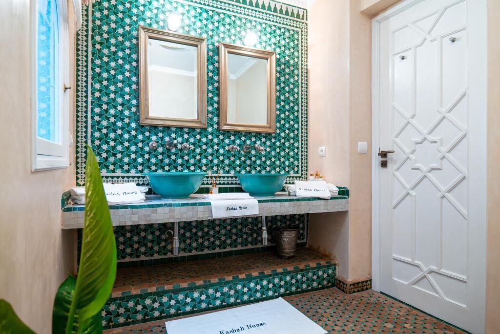 Casa de banho com painel de azulejos com padrão de estrelas verdes, dois espelhos e lavatório duplo.