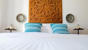Un lit avec du linge de lit blanc, deux coussins à motifs bleus et une tête de lit en bois sculptée.