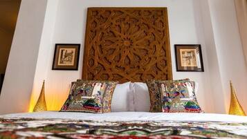 Una cama con un cabecero estampado, dos almohadas con diseños intrincados y cuadros enmarcados en la pared.