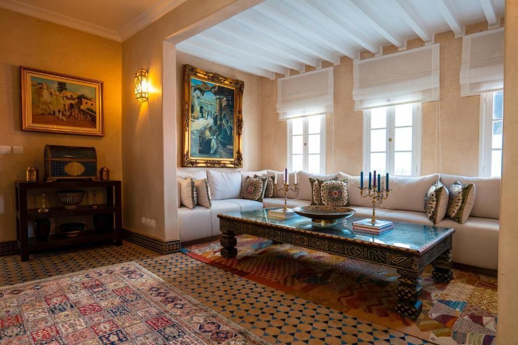 A cozy living room with a patterned rug, a sofa with cushions, a coffee table with a decorative centerpiece, and a painting on the wall.