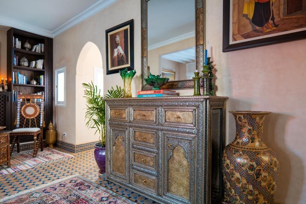 A room with a patterned floor, a large ornate cabinet, a bookshelf, and a large vase.