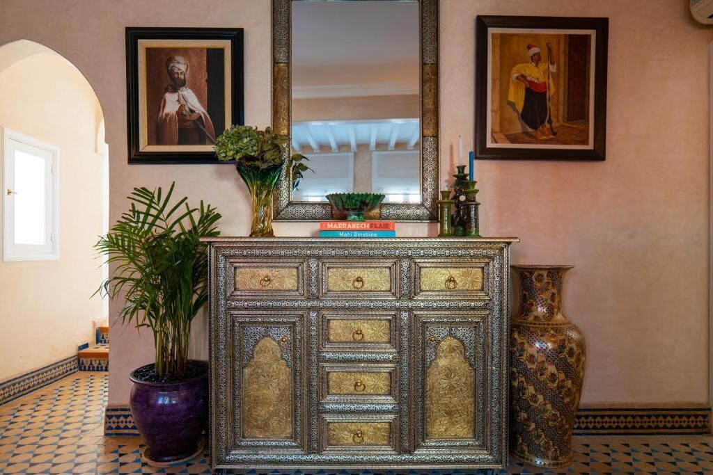 A hallway with a decorative cabinet, framed artwork, and a potted plant.