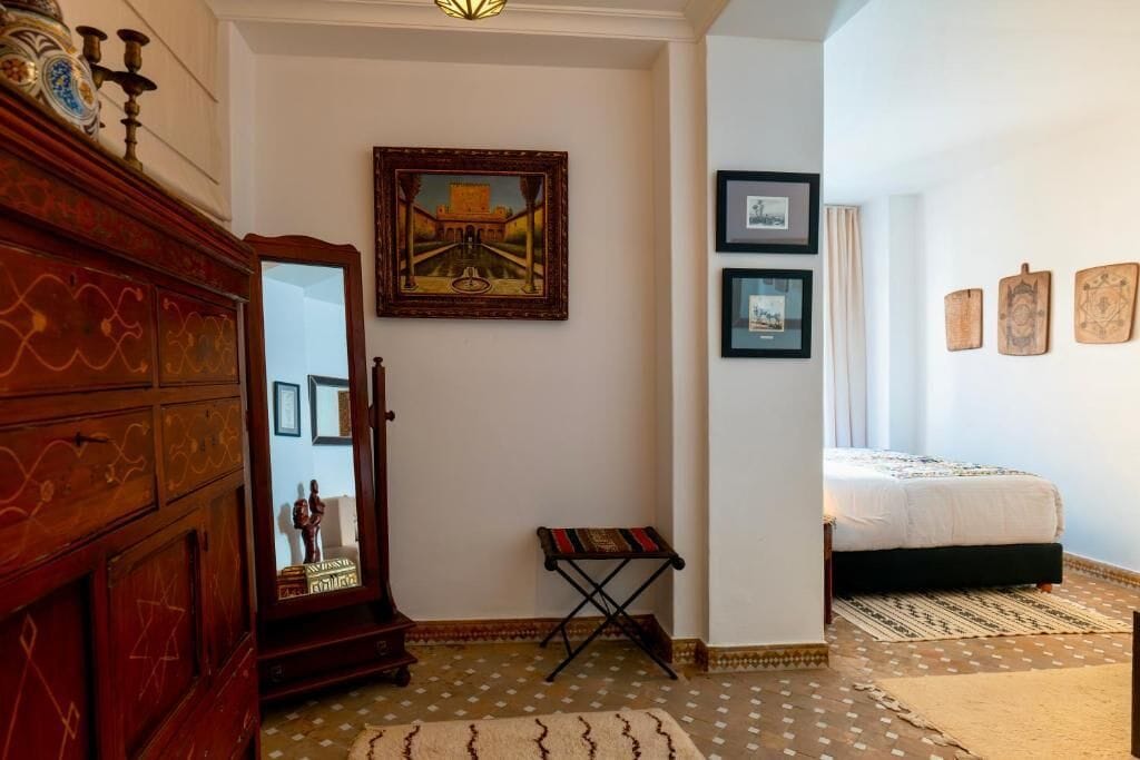 Un dormitorio con cama, cómoda de madera, espejo y un cuadro enmarcado en la pared.