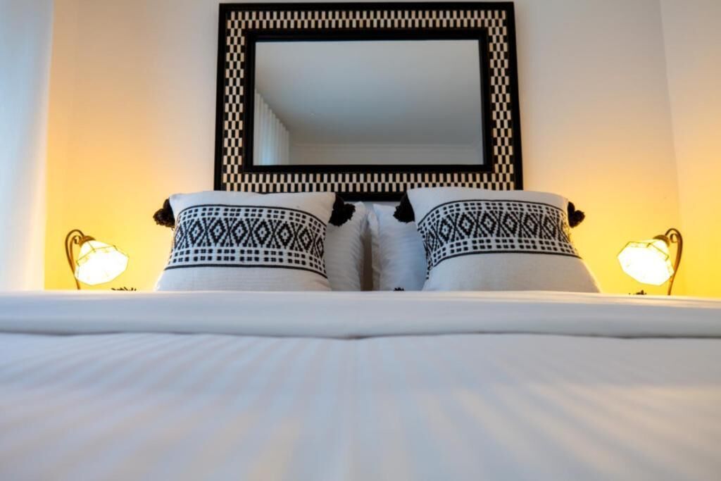A bed with patterned pillows and a large mirror above it.