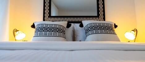 A bed with patterned pillows and a large mirror above it.