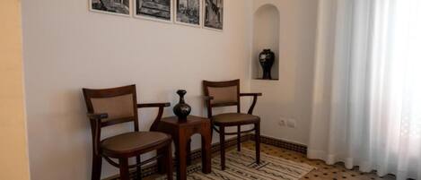 A room with a patterned rug, two wooden chairs, a small table, and three black-and-white framed pictures on the wall.