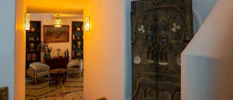 A staircase with a patterned floor leading to a room with a traditional door, a chandelier, and a view of a dining area.