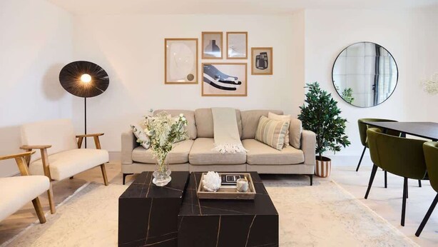 Ein modernes Wohnzimmer mit Sofa, Couchtisch, Stehlampe und gerahmten Kunstwerken an der Wand.