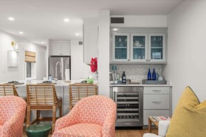 A modern kitchen with white cabinets, a stainless steel refrigerator, and a dining area with patterned chairs. - Beachfront Aldea 12, Designers Condo (Belleair Beach)