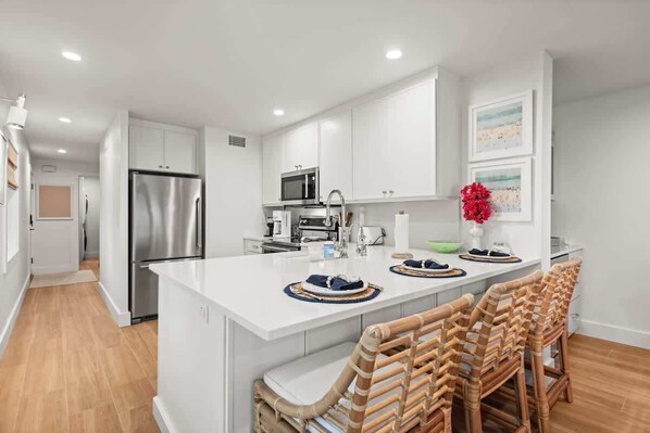 A modern kitchen with white cabinetry, stainless steel appliances, and a central island with bar seating.