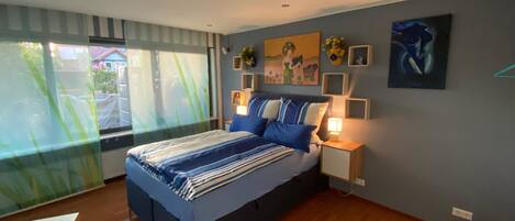 Un dormitorio con cama, mesitas de noche, una ventana con cortinas y decoración en la pared.