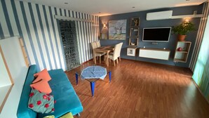 A modern living room with a striped wall, a blue sofa, a wooden dining table, and a TV mounted on the wall. - Ilonas Home (Baden-Baden)