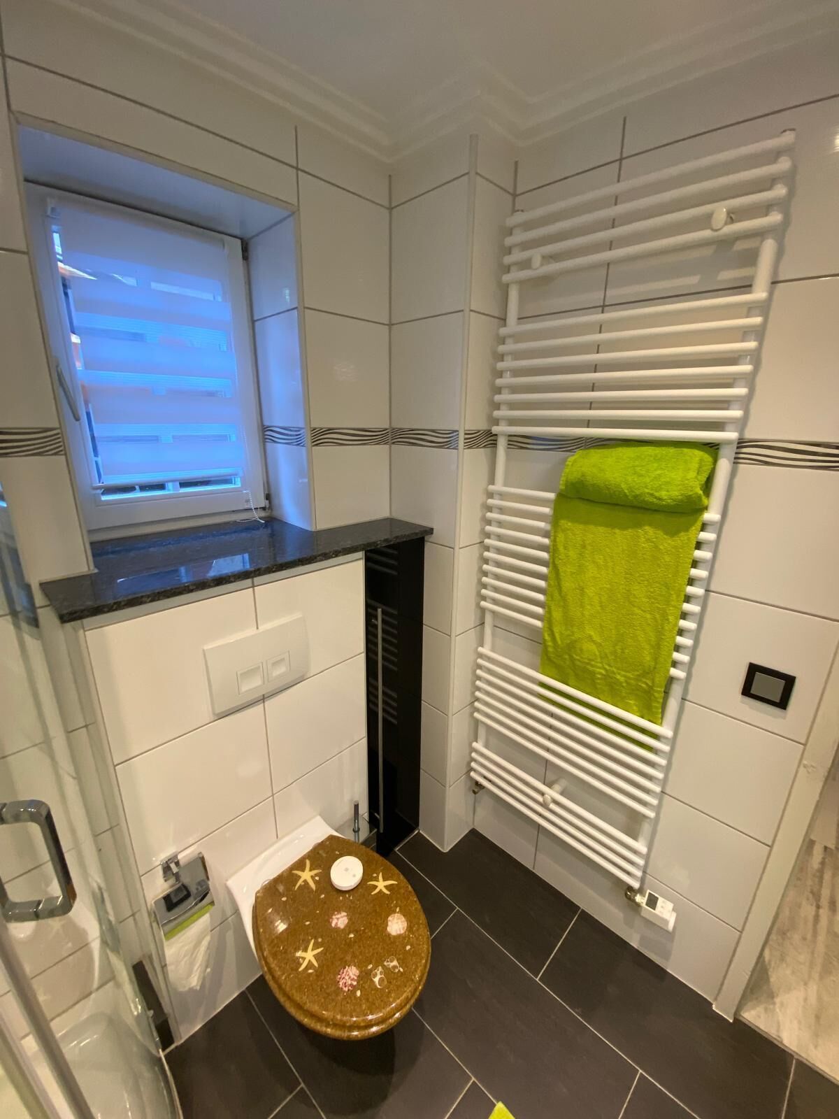 Ein Badezimmer mit Toilette, Fenster, Handtuchhalter und Duschbereich.