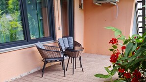 A patio with wicker furniture, a potted plant with red flowers, and a wall-mounted air conditioner. - Ilonas Home (Baden-Baden)