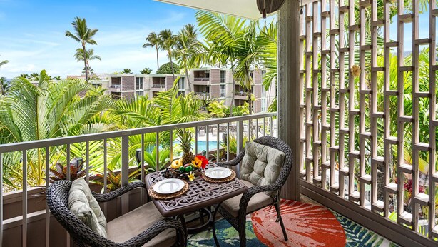 A balcony with wicker furniture, a table set for dining, and a view of palm trees and buildings.