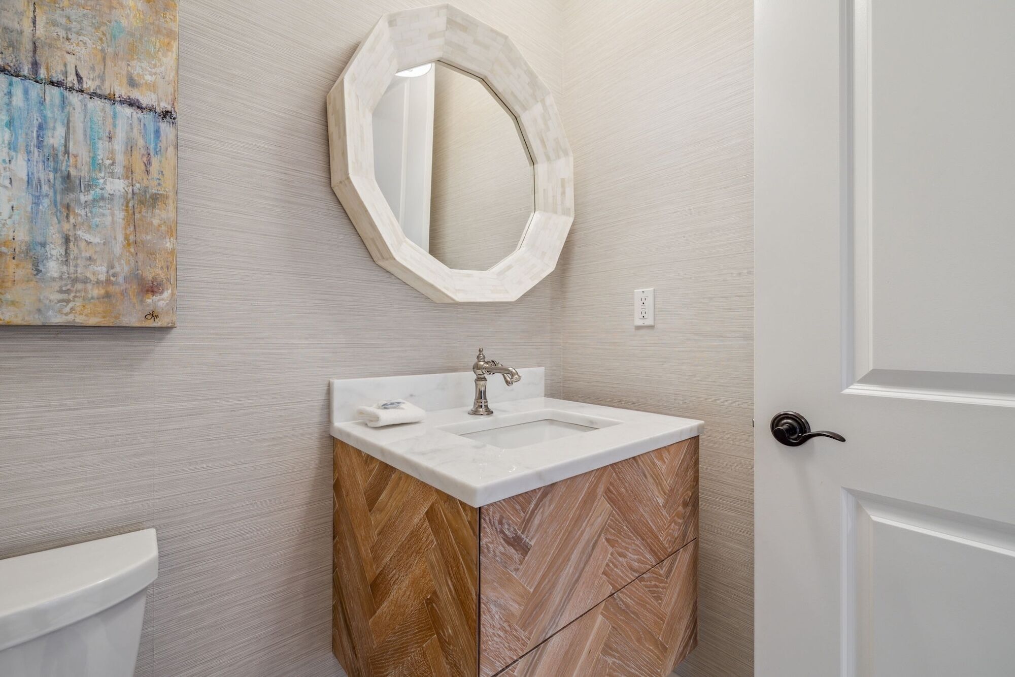 A bathroom with a white sink, a wooden cabinet, and a large mirror on the wall.