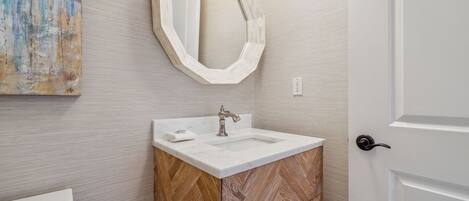 A bathroom with a white sink, a wooden cabinet, and a large mirror on the wall.