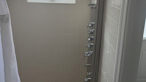 A shower with a handheld showerhead, a window with blinds, and a towel rack.