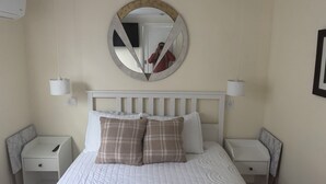 A hotel room with a large bed, two bedside tables, a round mirror, and a white headboard.