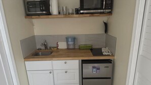 A compact kitchen with a wooden countertop, a stainless steel refrigerator, a dishwasher, and a microwave above the counter.