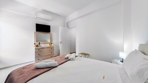 Ein modernes Hotelzimmer mit einem großen Bett, einem Holzschrank, einem Spiegel, einem Flachbildfernseher und einem Nachttisch mit Lampe.