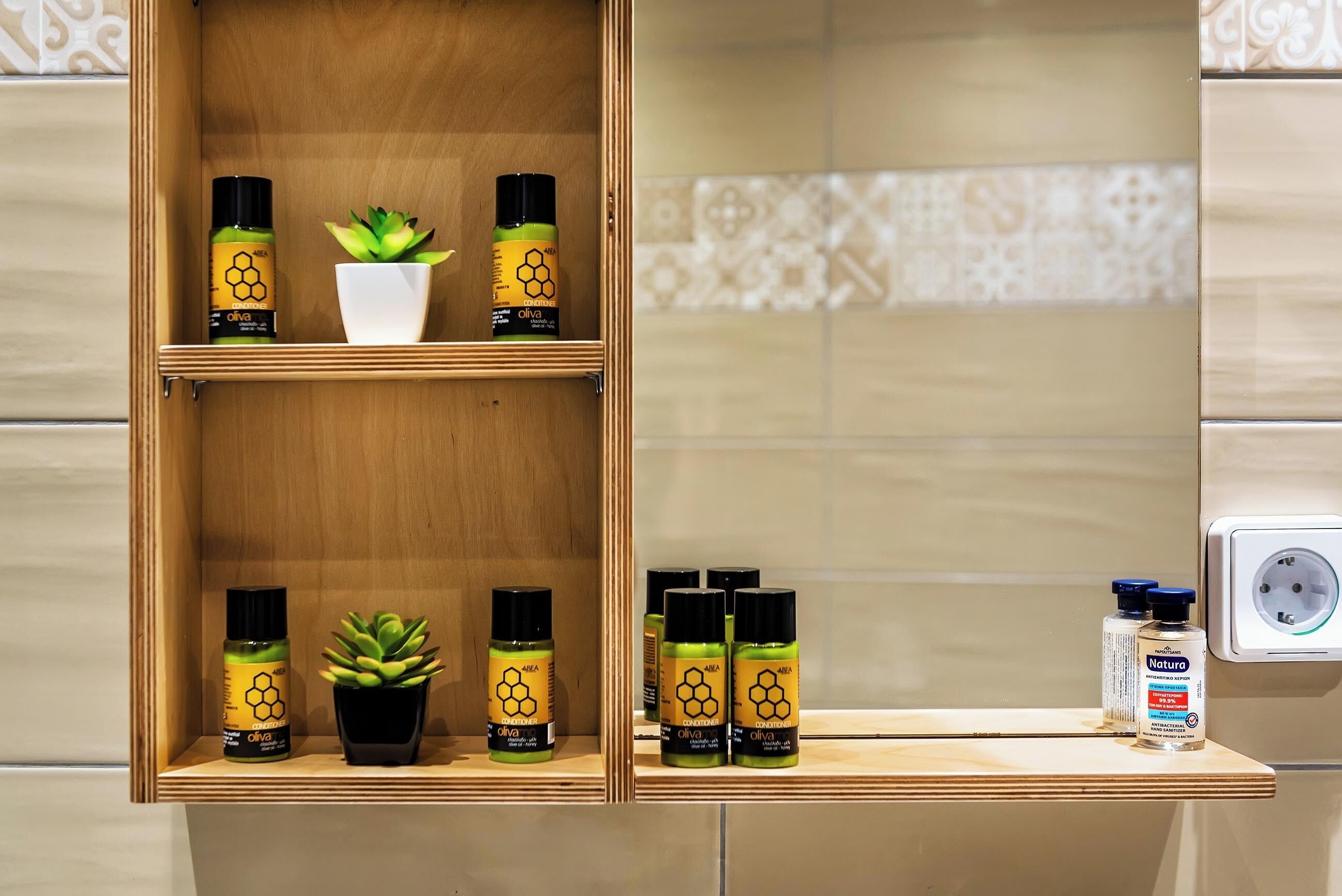 A bathroom shelf with olive oil bottles, a potted plant, and a bottle of Natura.
