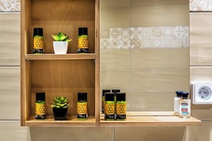 A bathroom shelf with olive oil bottles, a potted plant, and a bottle of Natura. - Grekodes 7 (Heraklion)