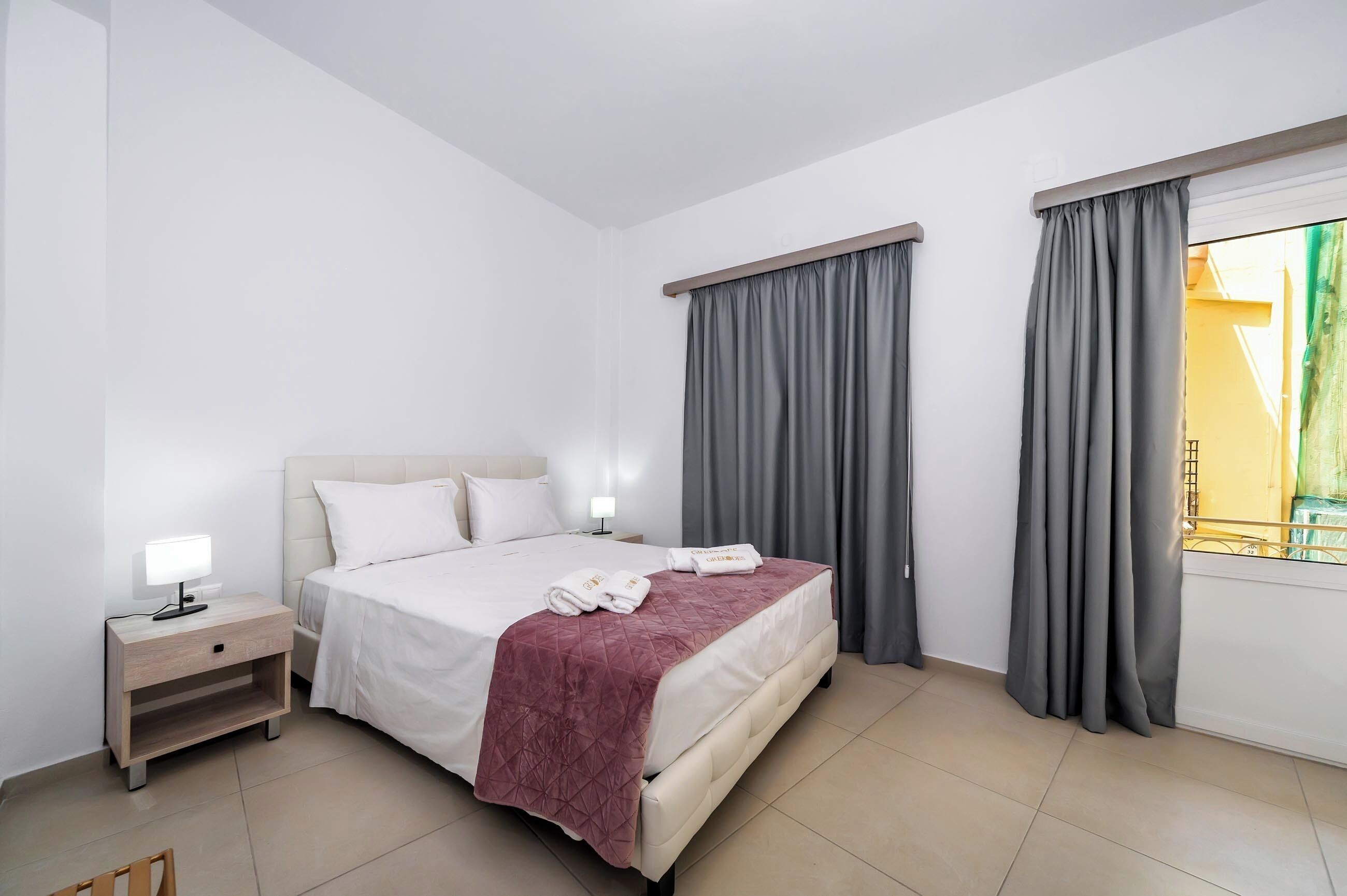 Habitación de hotel con cama, mesita de noche y cortinas.
