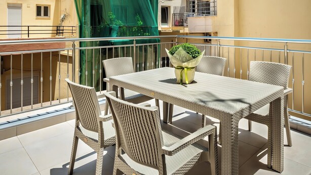 Ein Balkon mit Tisch und Stühlen, einem grünen Vorhang und einem Gebäude im Hintergrund.