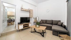 Ein modernes Wohnzimmer mit Sofa, Fernseher, Couchtisch und einem Essbereich mit Stühlen und Tisch.