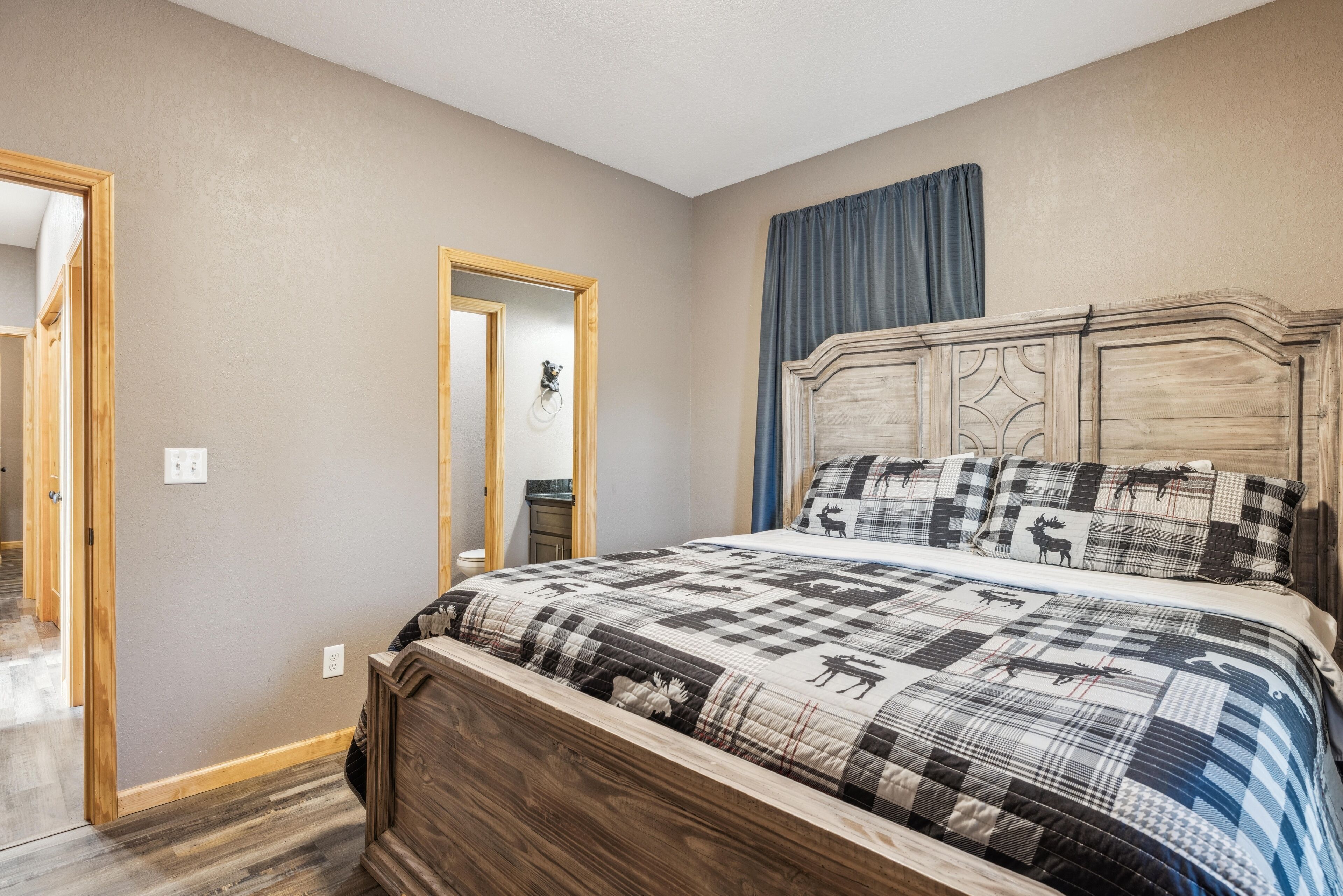 Un dormitorio con estructura de cama de madera, colcha acolchada con estampados de animales, un espejo y una puerta que da a otra habitación.
