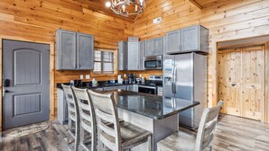 A wooden cabin interior with a kitchen featuring grey cabinets, a central island with chairs, a chandelier, and a large wooden door. - Wild Heart Lodge 4 Bedroom Cabin (Sevierville)