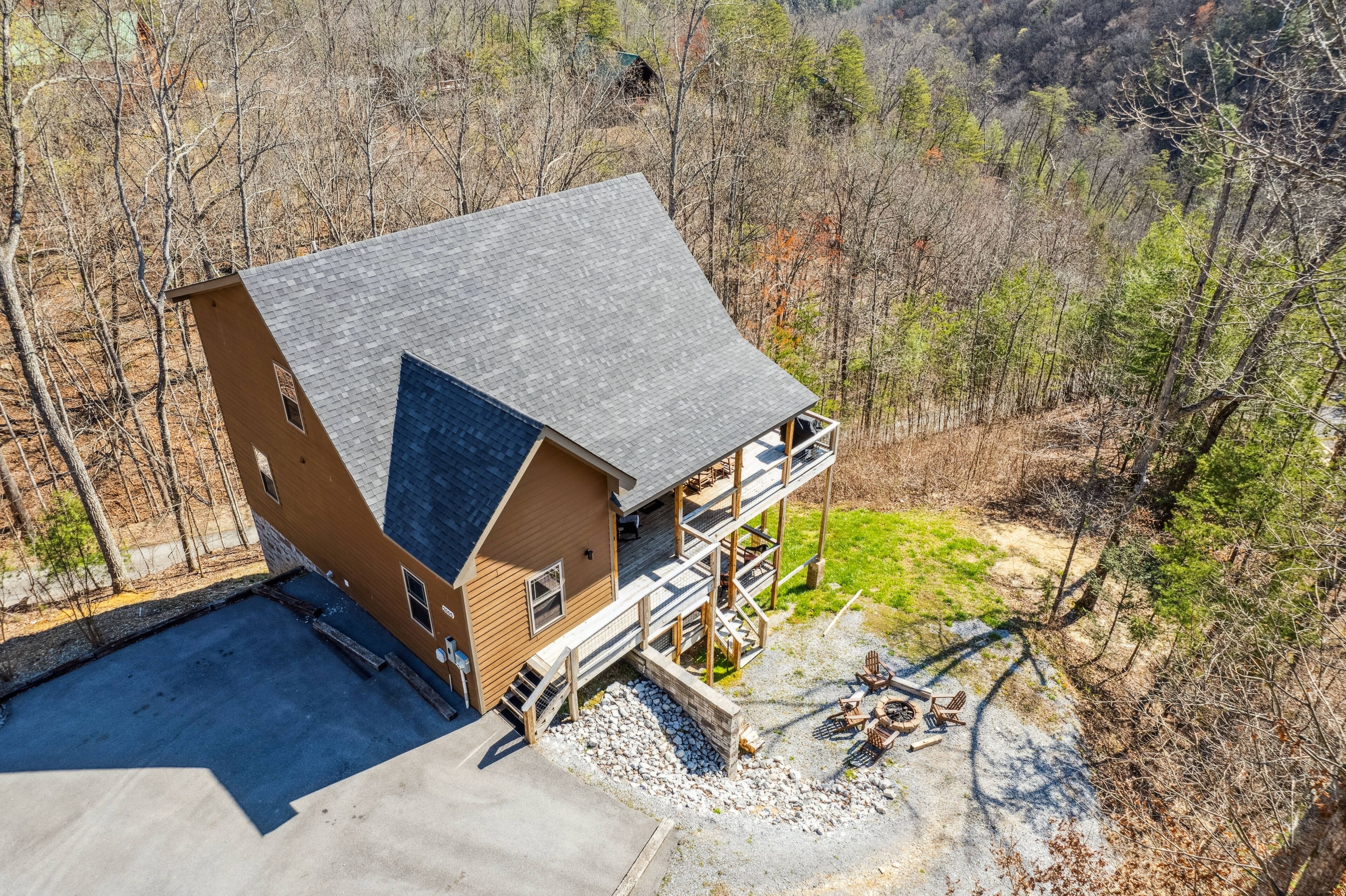A two-story cabin with a balcony, surrounded by trees and a gravel driveway.