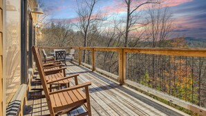 A wooden deck with chairs and a table, overlooking a forested area with autumn foliage. - Wild Heart Lodge 4 Bedroom Cabin (Sevierville)